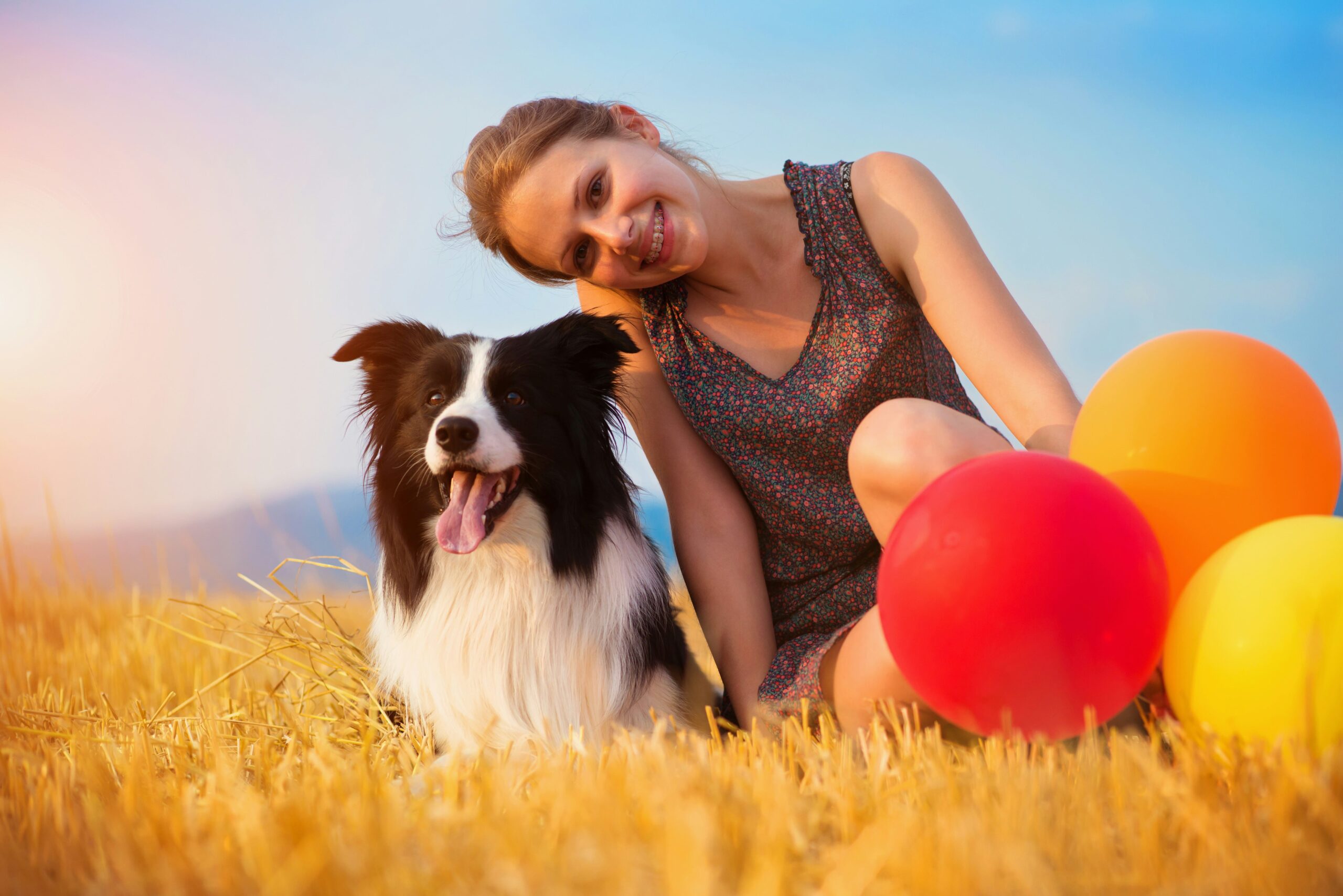 A girl sitting with a dog smiling and baloons around
